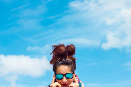 brunette girl with blue glasses and a big messy bun, red lips and nails with the sky as backgroundの写真素材