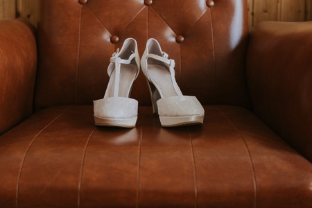 white lace bridal shoes on top of a brown leather vintage sofaの写真素材