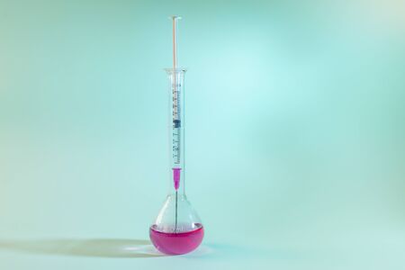 a syringe inside of a test tube on blue background. Experiment, medicine and science concept.