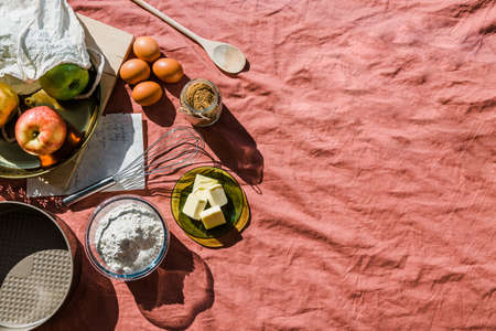 flat lay of baking ingredients arranged on a pink tablecloth for making an apple pie