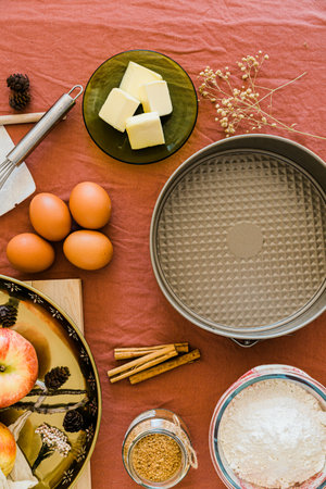 Vertical flat lay of baking ingredients arranged on a pink tablecloth for making an apple pie