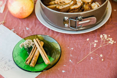 Close up of cinnamon sticks and a piece of paper with a recipe and a cake as a background. Pink tableclothの写真素材