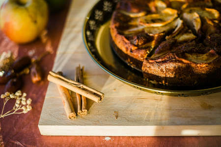 detail of cinnamon sticks on a wooden board next to an apple cakeの写真素材