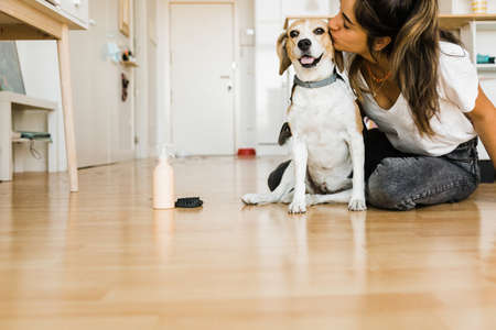 young woman kissing her dog on the floorの写真素材