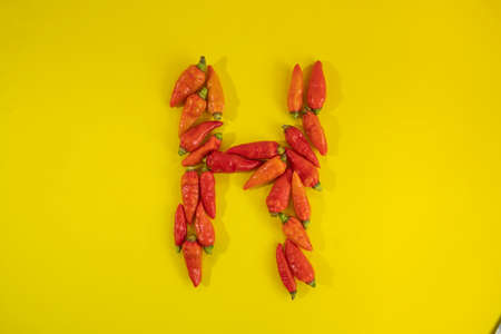 red pepper isolated on a yellow background. red chili peppers forming letter H pattern isolated on yellow backgroundの写真素材
