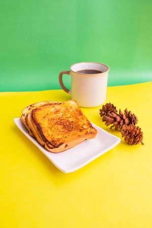 Toast On A White Plate And Black Coffee Mug With Spruce Flowers On A Yellow And Green Paper...