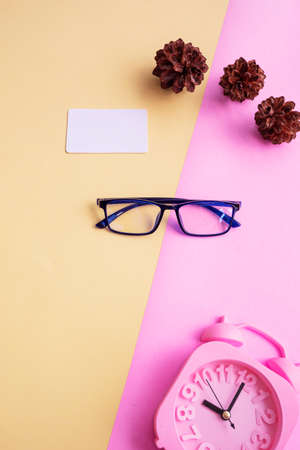 square glasses on a pink and yellow background with additional accessories an alarm clock and pine tree flowers. minimal summer styleの写真素材