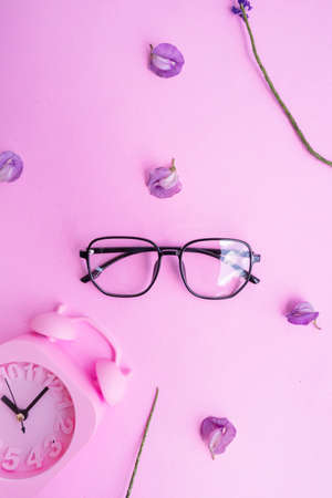 pentagonal glasses in the photo in minimal summer style on a pastel pink color background. alarm clock purple flowerの写真素材