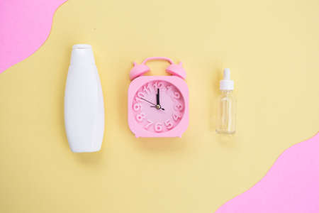 Beauty background of cosmetic bottles and alarm clock on yellow and pink paper background. Summer skin care conceptの写真素材