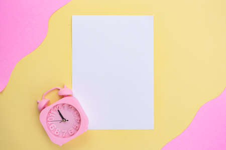 white paper and alarm clock on yellow and pink background. minimalist style