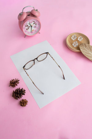 Cat's eye glasses in the photo from above with a minimalist concept on a purple paper background with an alarm clock decoration and dry leavesの写真素材