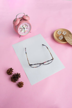 Cat's eye glasses in the photo from above with a minimalist concept on a purple paper background with an alarm clock decoration and dry leavesの写真素材