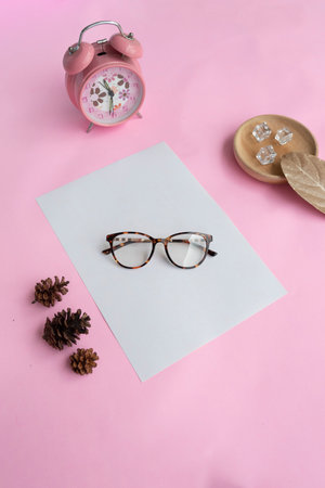 Round glasses in the photo from above with minimalist concept on purple paper background with alarm clock decoration, dry leaves and fir tree flowersの写真素材