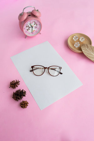 Round glasses in the photo from above with minimalist concept on purple paper background with alarm clock decoration, dry leaves and fir tree flowersの写真素材