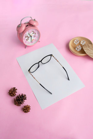 Round glasses in the photo from above with minimalist concept on purple paper background with alarm clock decoration, dry leaves and fir tree flowersの写真素材