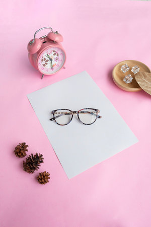 Round glasses in the photo from above with minimalist concept on purple paper background with alarm clock decoration, dry leaves and fir tree flowersの写真素材