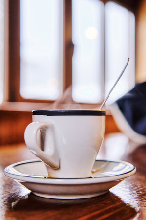 Hot Espresso coffee cup with coffee set spoon and plate on wood table with window at background on mountain barの写真素材