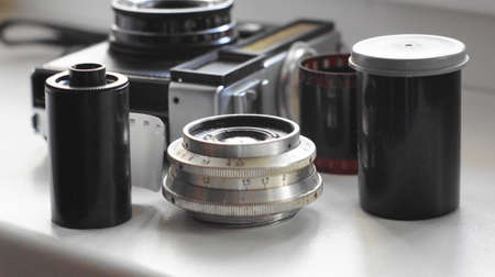 Accessories from old film cameras. A still life of accessories from old film camera: camera, lens, film cassette, piece of film, film containerの写真素材