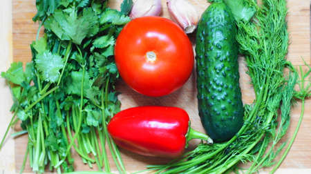 Still life with vegetables. A set of vegetables consisting of tomato, cucumber, bell pepper, parsley, dill and garlic. This is on the cutting board.の写真素材