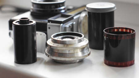 Accessories from old film cameras. A still life of accessories from old film camera: camera, lens, film cassette, piece of film, film container.の写真素材