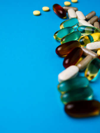 Spilled colored medications and pills on a blue background. Pharmacology and medicine struggle for health. Drug addiction. Treatment of various diseasesの写真素材
