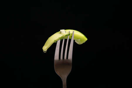 Slice of fresh green cucumber on fork on dark black background.の写真素材