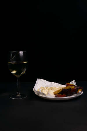 glass of wine next to a slice of cheese, plums with a black backgroundの写真素材