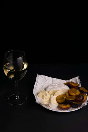 glass of wine next to a slice of cheese, plums with a black backgroundの写真素材