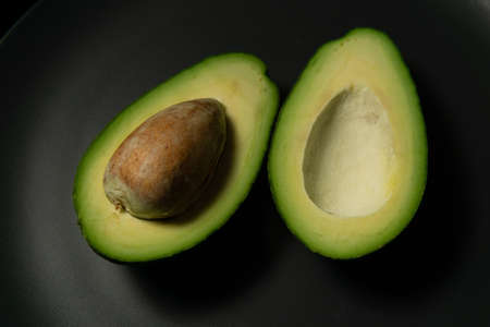 Fresh, raw avocado sliced on a black plate on a gray background