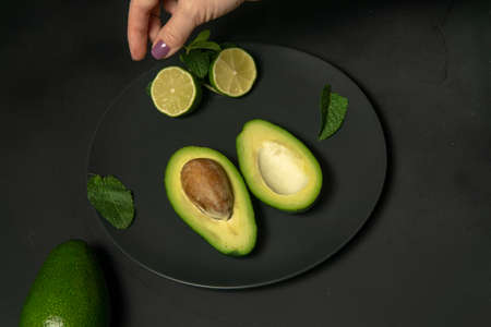 Avocado with limes on a black plate on a dark backgroungの写真素材