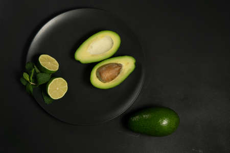 Avocado with limes on a black plate on a dark backgroungの写真素材