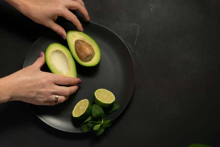 Woman preparing raw avocado and lime on a black plate on a dark backgroungの写真素材