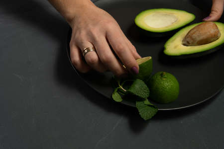 Woman preparing raw avocado and lime on a black plate on a dark backgroungの写真素材