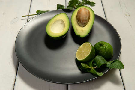 Avocado with limes on a black plate on a white wooden backgroungの写真素材