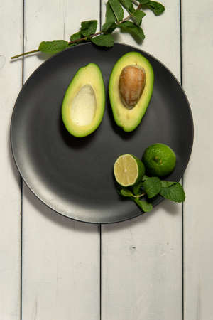 Avocado with limes on a black plate on a white wooden backgroungの写真素材
