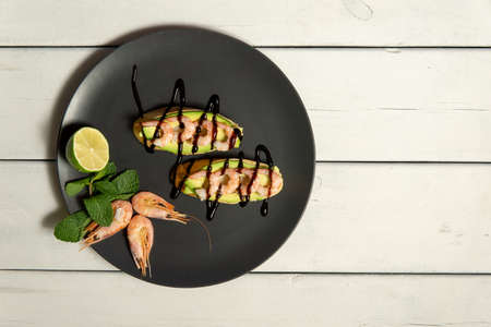 bruschetta with shrimps, avocado and lime on a dark plate on a white wooden backgroundの写真素材