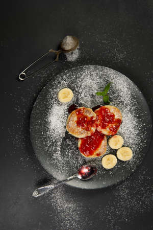 Cottage cheese pancakes on a black plate sprinkled with powdered sugar. Homemade food. Syrniki with fresh mint.の写真素材