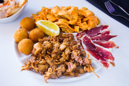 Plate with different tapas. Bravas potatoes, ham, fried squid and croquettes.