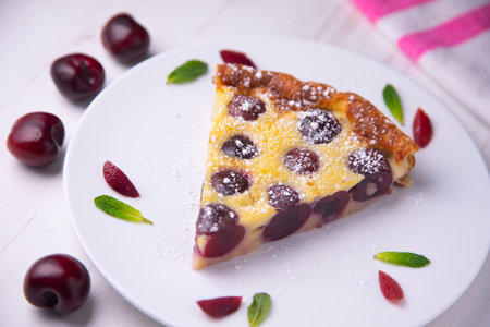 Cherry clafoutis is a baked French fruit dessert, traditionally black cherries, arranged on a...