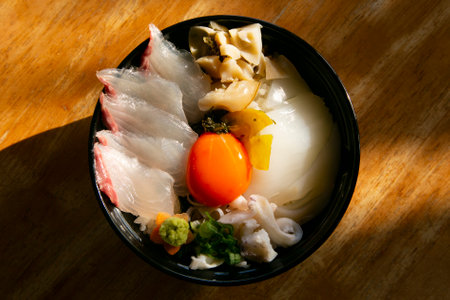 Japanese sashimi donburi with white fish, squid and egg yolk on a bed of white rice.の写真素材