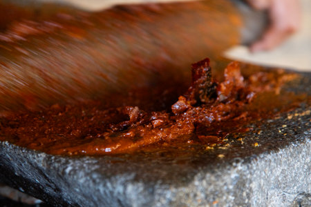 Woman from an indigenous community in Oaxaca preparing traditional red mole with a metate, a tool for grinding ingredients in Mexico.の写真素材