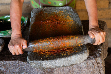 Woman from an indigenous community in Oaxaca preparing traditional red mole with a metate, a tool for grinding ingredients in Mexico.の写真素材