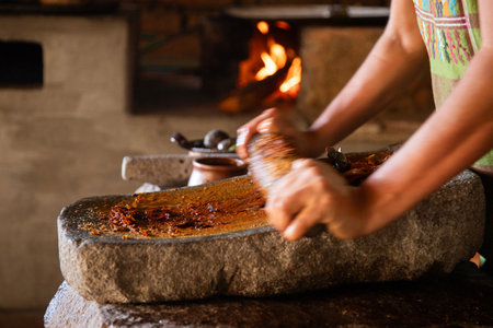 Woman from an indigenous community in Oaxaca preparing traditional red mole with a metate, a tool...