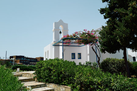A white church with a bell tower and a blue archway. The archway is covered in pink flowers