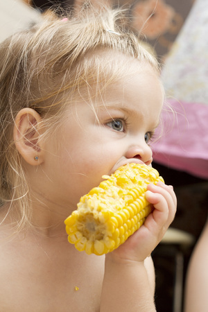 Little cute blonde babygirl eating boiled cornの写真素材