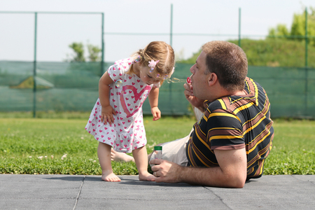 Happy family playing with their daughter with bubbles outside in the parkの写真素材