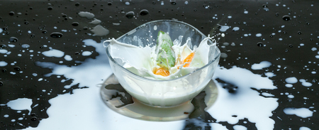 Fruits splashing milk in a round bowl on a black backgroundの写真素材