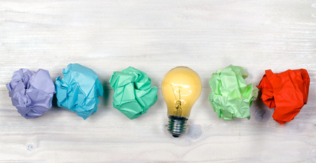 Tungsten lightbulb on a wooden textured background along with different coloured paperの写真素材