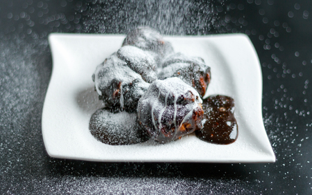 Profiterole pieces on a white plate covered with chocolate cream and powder sugarの写真素材