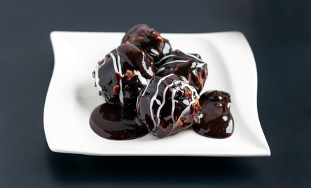 Profiterole pieces on a white plate covered with chocolate cream and powder sugar